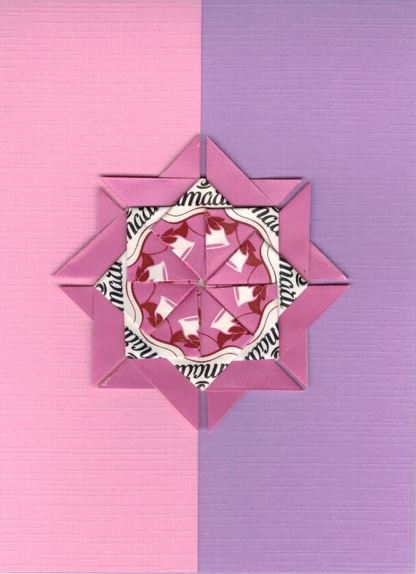 Een wit roze rozet op een kaart met lichtpaars bladwijzer motief. <br>Deze rozet is gemaakt uit Amarti harmony theezakjes.