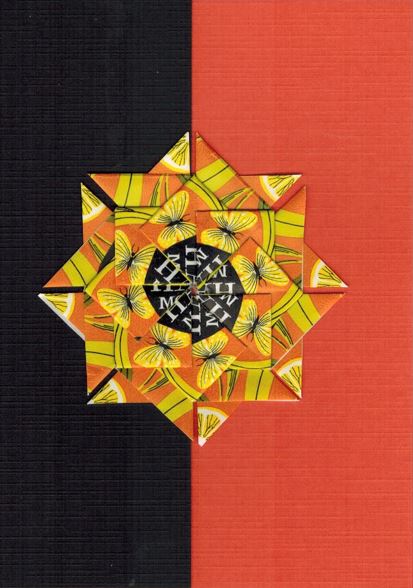 Een geel oranje rozet met zwarte kern op een kaart met bladwijzer motief. <br>Deze rozet is gemaakt uit een deel van oranje Clipper theezakjes.