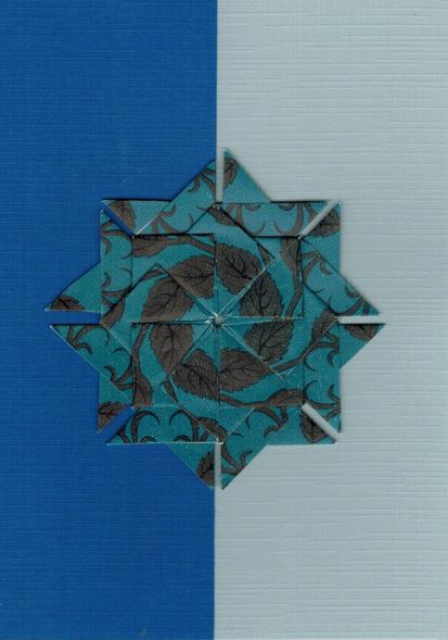 Een donkerblauwe  rozet met grijze design op een kaart met bladwijzer motief.<br>Deze rozet is gemaakt uit Clipper snore and peace theezakjes.